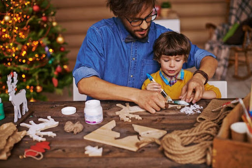 father and son painting together, brown table, twine, blue shirt